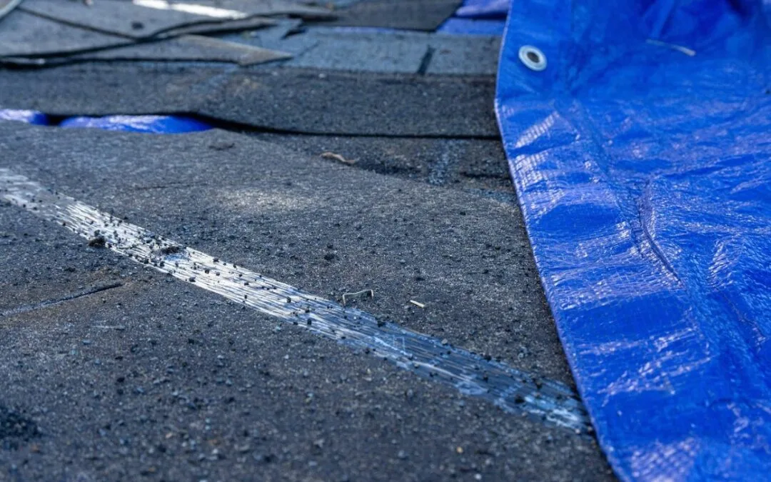 Poorly installed roof showing damaged shingles and exposed underlayment with blue tarp protection.