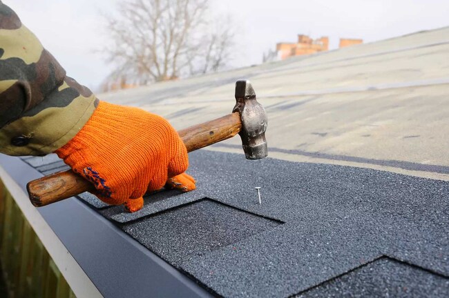 Roof shingle repair in progress with a roofer fixing asphalt shingles on a residential roof in New Jersey