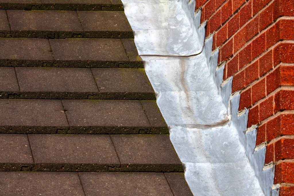 Detailed view of roof flashing repair between shingles and brick wall on a residential home in New Jersey.